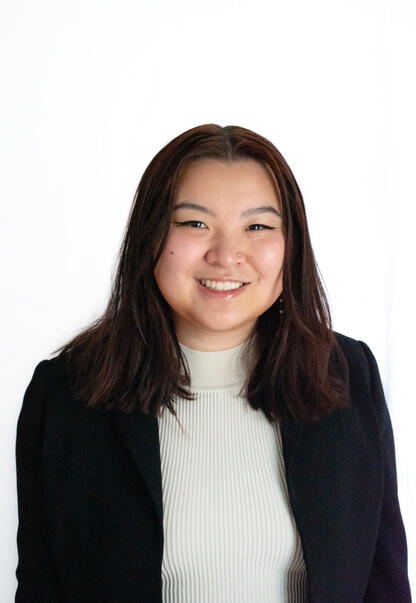 A photo of an Asian feminine person smiling with medium-length dark brown/red hair.